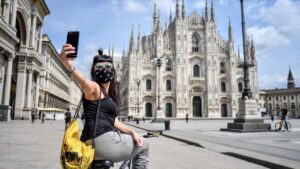 Una mujer con mascarilla se hace un selfie frente a la catedral de Milán